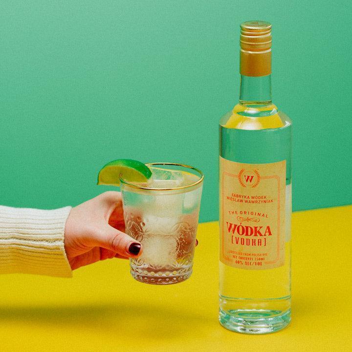 Wódka üveg, mellette egy kéz tartja a koktélos poharat, sárga és zöld háttérrel