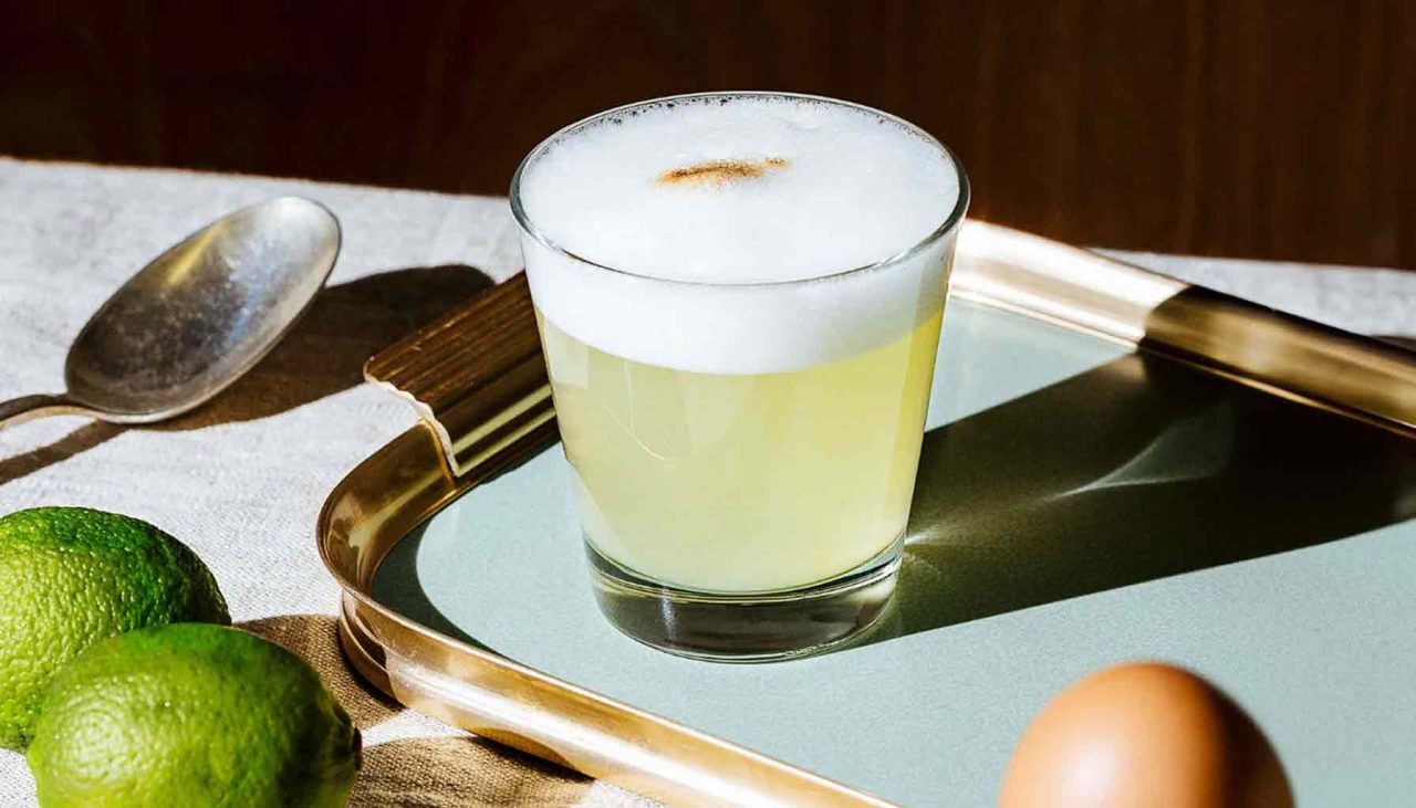 Egy elegáns pohárban szervírozott Pisco Sour, frissen facsart lime és cukorszirup felhasználásával, habos tojásfehérje réteggel a tetején.